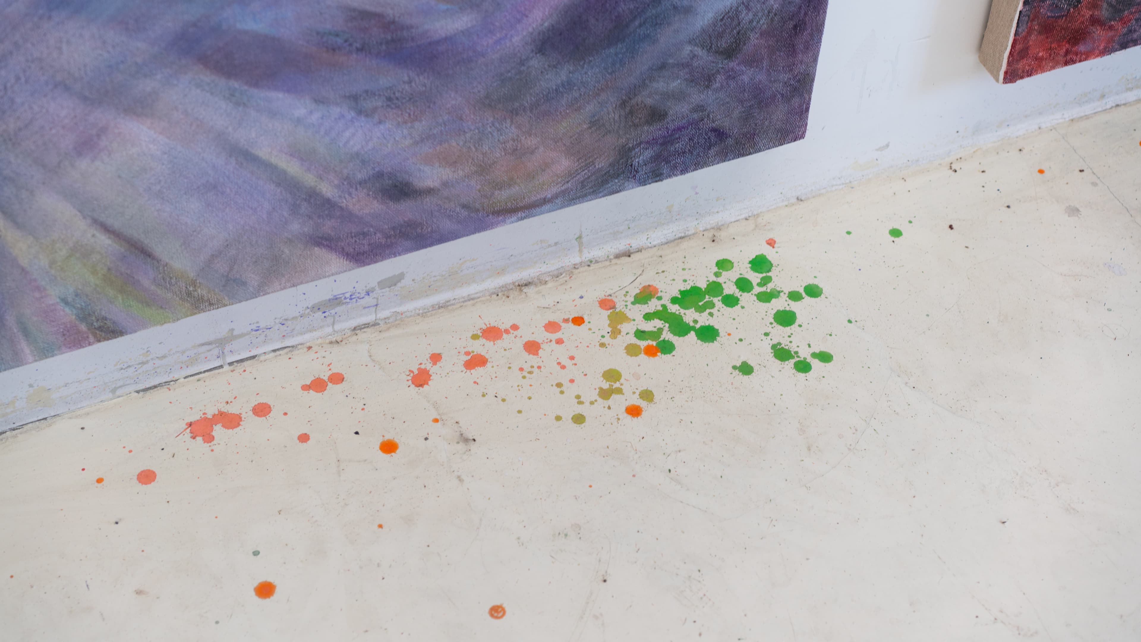 Bright paint splatters on the floor beside a canvas in Xiaofu Wang's studio